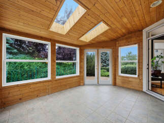 Experience seamless indoor-outdoor living in this charming sunroom, featuring a warm wood-paneled interior and a vaulted ceiling with skylights.