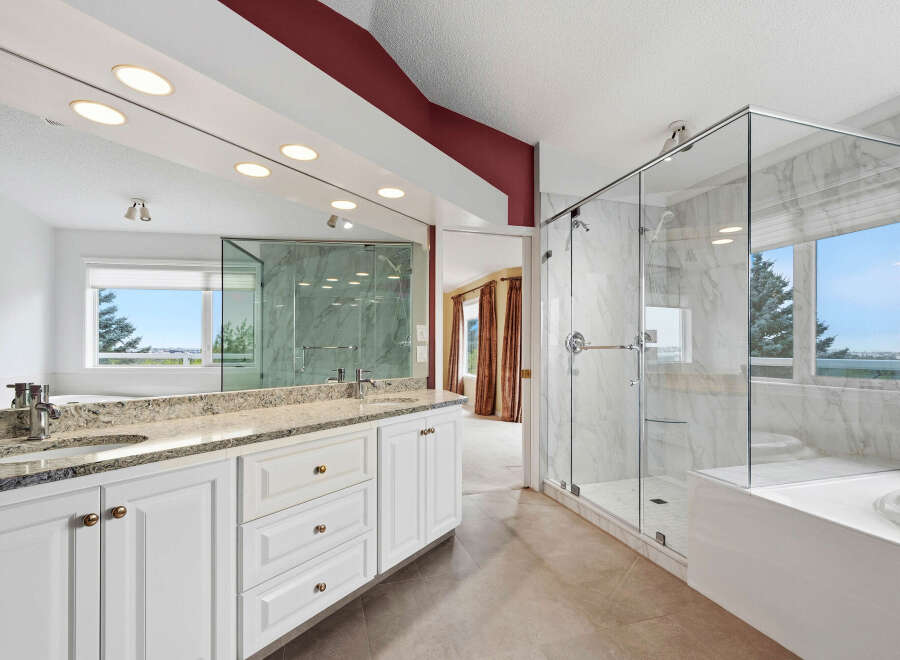 Experience luxury in this stunning master bathroom, featuring a spacious glass-enclosed marble shower and a deep soaking tub with a scenic view.