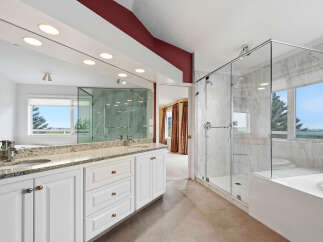 Experience luxury in this stunning master bathroom, featuring a spacious glass-enclosed marble shower and a deep soaking tub with a scenic view.