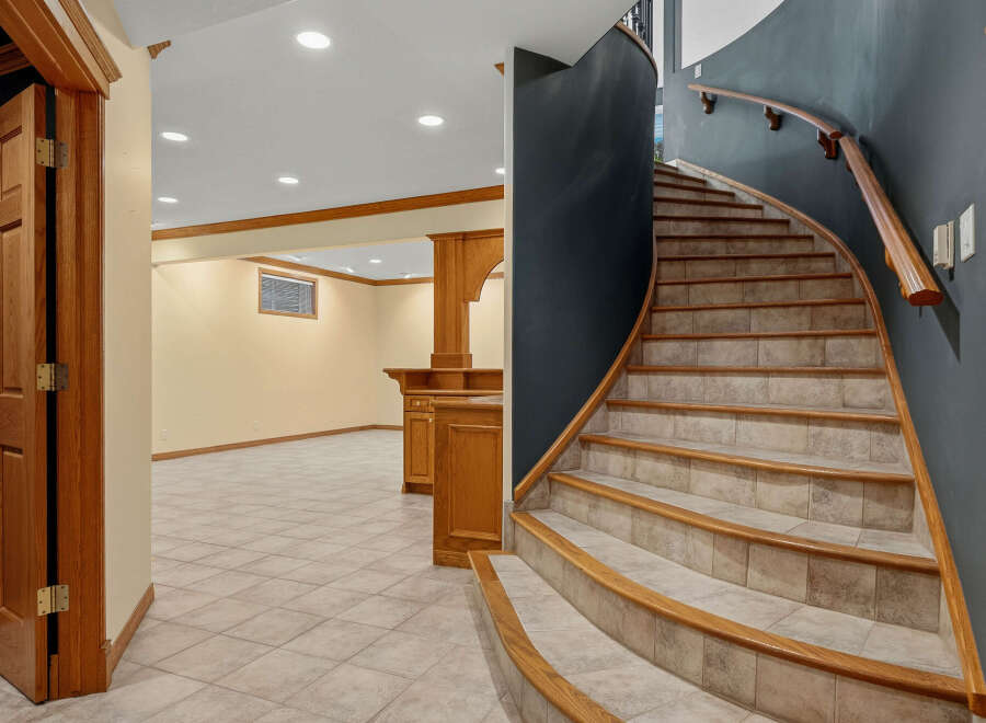 Discover this inviting basement space featuring a curved staircase with a wooden handrail and tiled steps, leading to a finished living area.