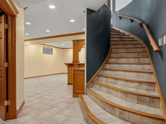 Discover this inviting basement space featuring a curved staircase with a wooden handrail and tiled steps, leading to a finished living area.