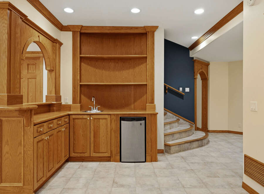 This stunning basement features a custom oak wet bar with a built-in sink, mini-fridge, and ample cabinet space, perfect for entertaining.