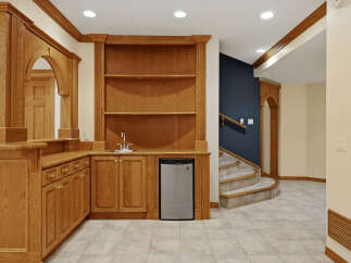 This stunning basement features a custom oak wet bar with a built-in sink, mini-fridge, and ample cabinet space, perfect for entertaining.