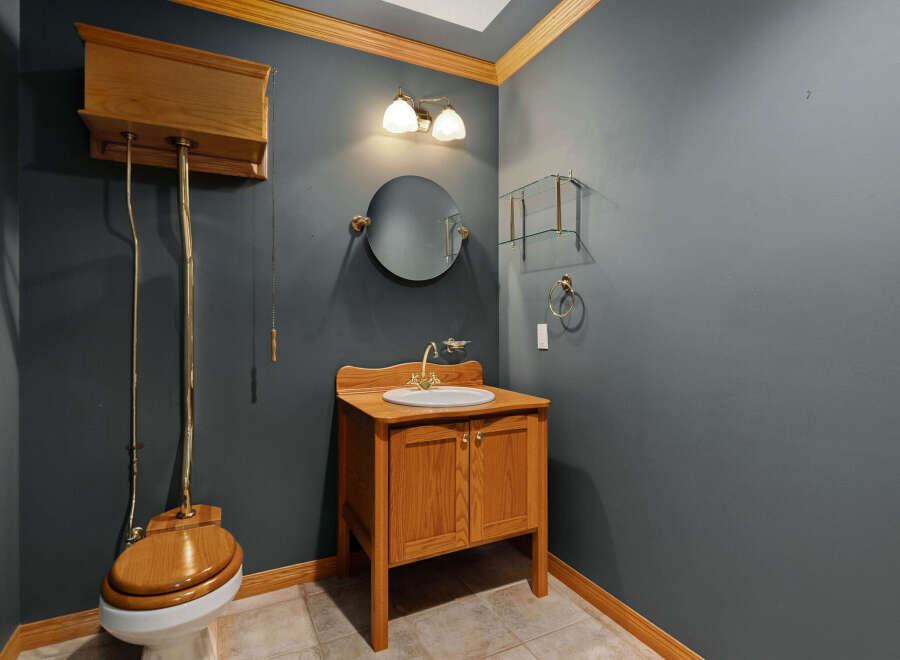 This charming bathroom features a classic high-tank toilet with a wooden seat and a matching wooden vanity with a white sink.