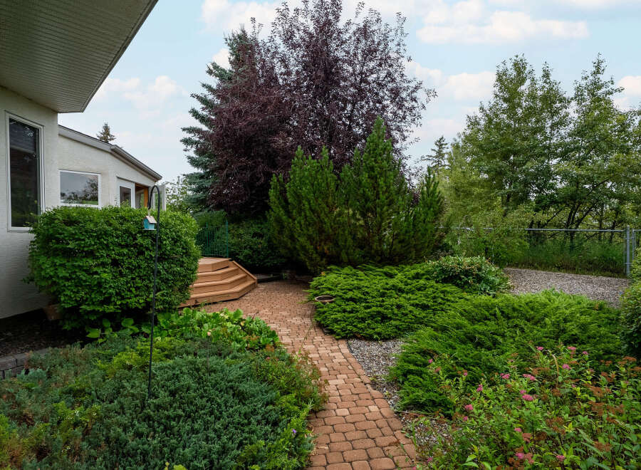 Discover a beautifully landscaped backyard featuring a charming brick pathway winding through lush greenery and mature trees.