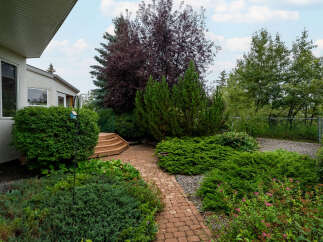 Discover a beautifully landscaped backyard featuring a charming brick pathway winding through lush greenery and mature trees.