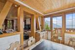 Experience breathtaking mountain views from this charming wooden chalet, featuring a cozy dining area with rustic wooden chairs and a large window overlooking the stunning landscape.