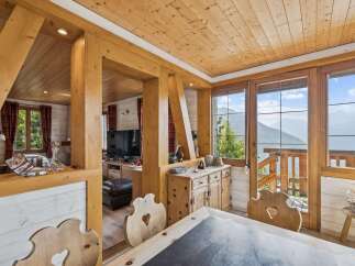 Experience breathtaking mountain views from this charming wooden chalet, featuring a cozy dining area with rustic wooden chairs and a large window overlooking the stunning landscape.