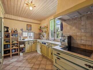 Discover this charming kitchen featuring light yellow cabinetry with contrasting green trim, complemented by a warm, tiled backsplash and a rustic wooden ceiling.