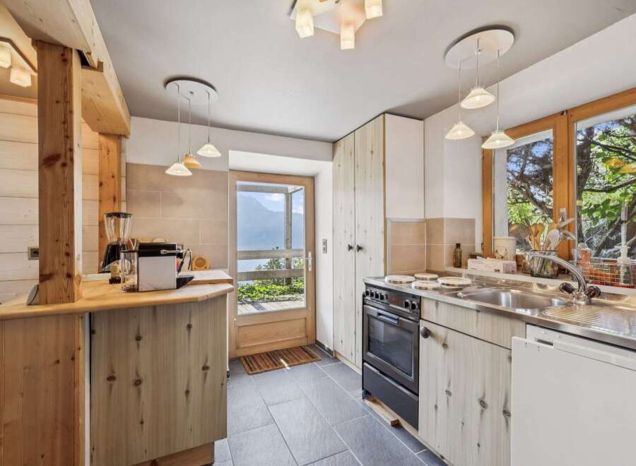 Experience rustic charm in this cozy kitchen featuring natural wood cabinetry and a stunning view of the mountains through the glass door.