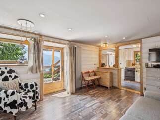 Experience cozy living in this charming mountain retreat, featuring a unique cow-print armchair and a rustic wooden interior.