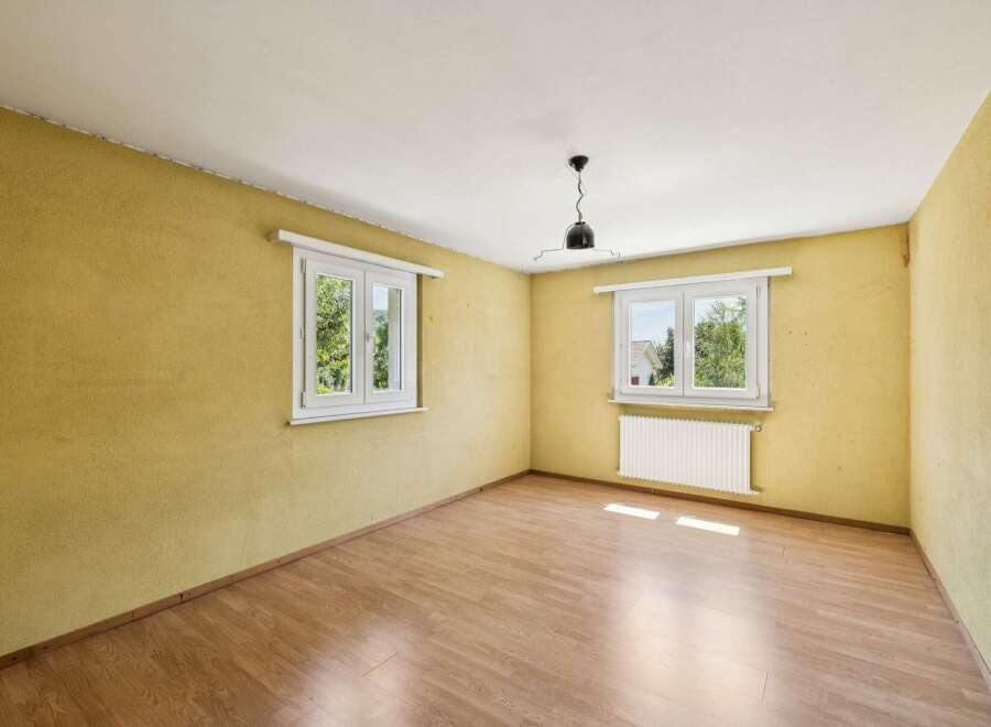 This empty room features a warm yellow textured wall and a light wood laminate floor, creating a cozy atmosphere.