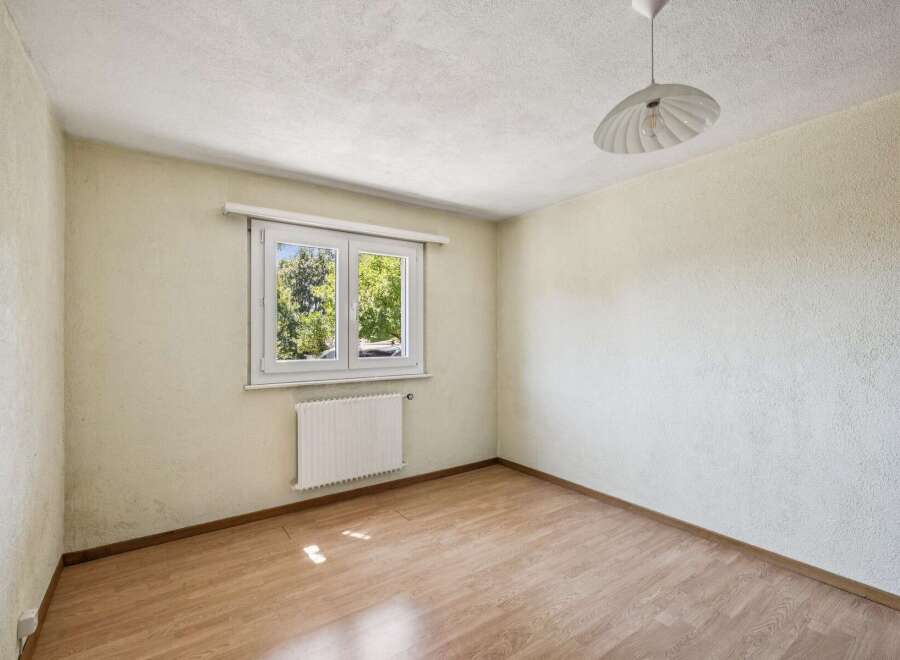 This empty room features a large window with a view of lush green trees, flooding the space with natural light.