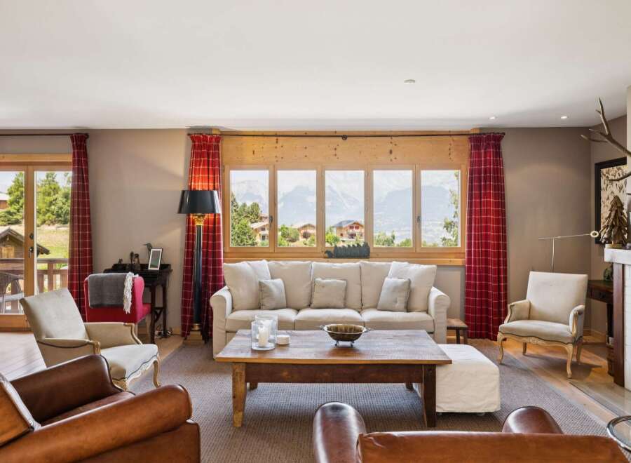 Experience breathtaking mountain views from this stunning living room, featuring a large sectional sofa and a rustic wooden coffee table.