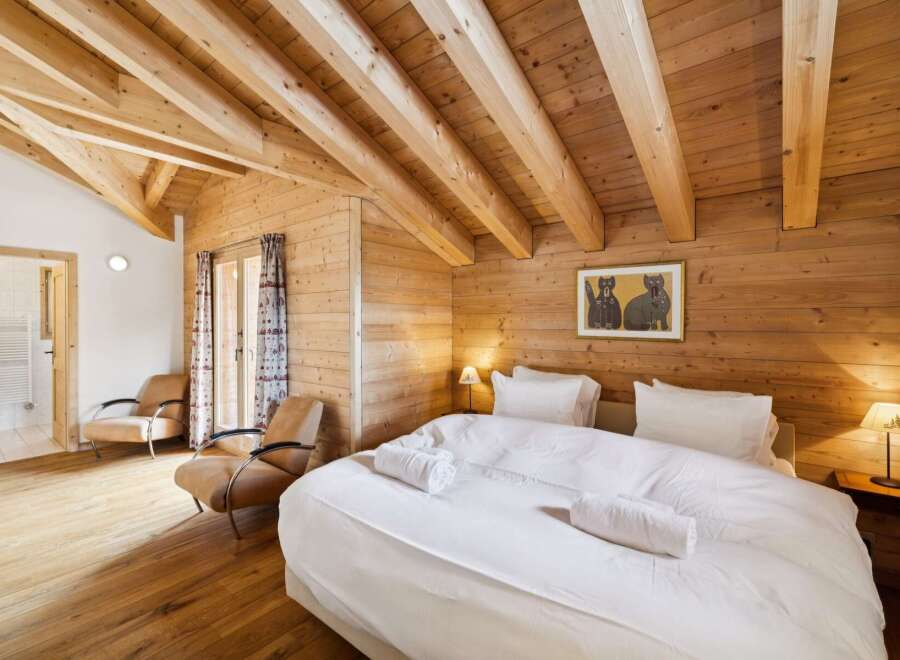 Experience rustic charm in this beautifully appointed bedroom, featuring exposed wooden beams and warm wood paneling throughout.