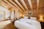 Experience rustic charm in this beautifully appointed bedroom, featuring exposed wooden beams and warm wood paneling throughout.
