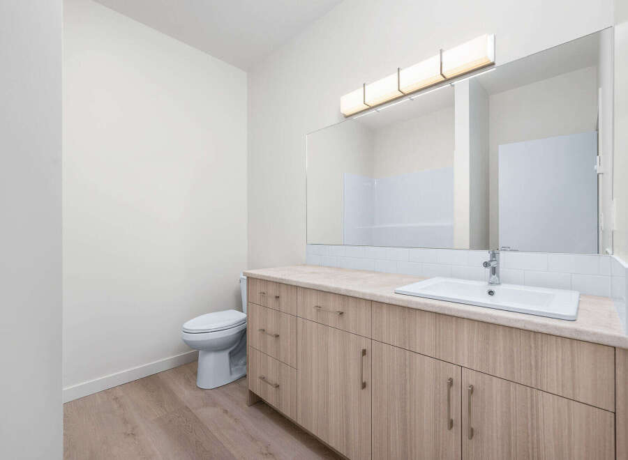 This modern bathroom features a sleek vanity with ample storage and a clean white sink, complemented by a large, illuminated mirror.