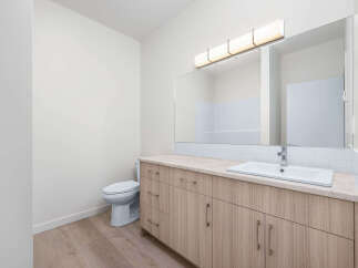 This modern bathroom features a sleek vanity with ample storage and a clean white sink, complemented by a large, illuminated mirror.