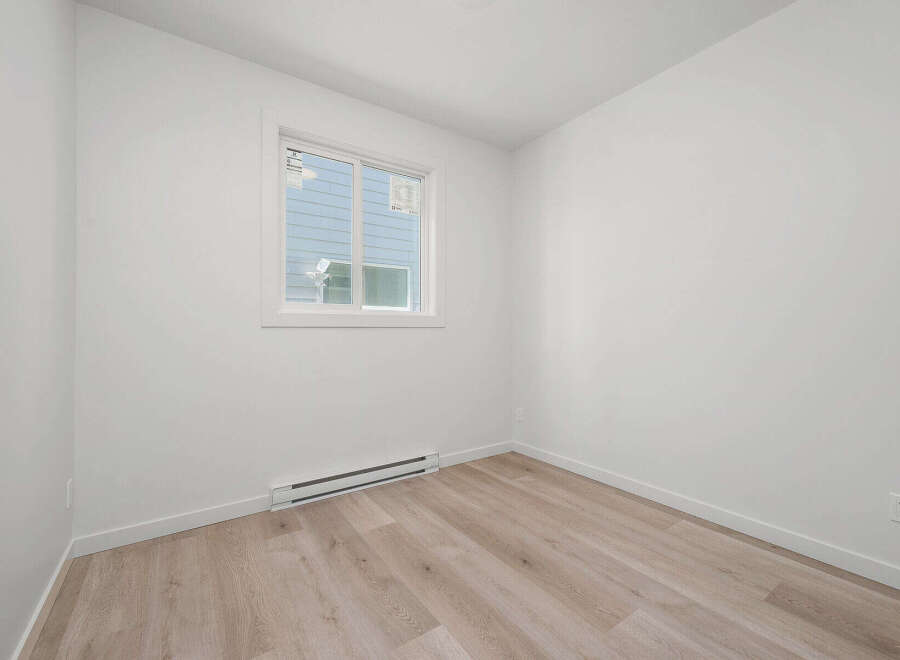 This bright and airy room features a large window that floods the space with natural light, complemented by clean white walls and modern light wood flooring.