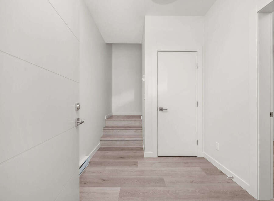 Step into a bright and modern entryway featuring sleek white doors and a convenient staircase leading to the upper level.