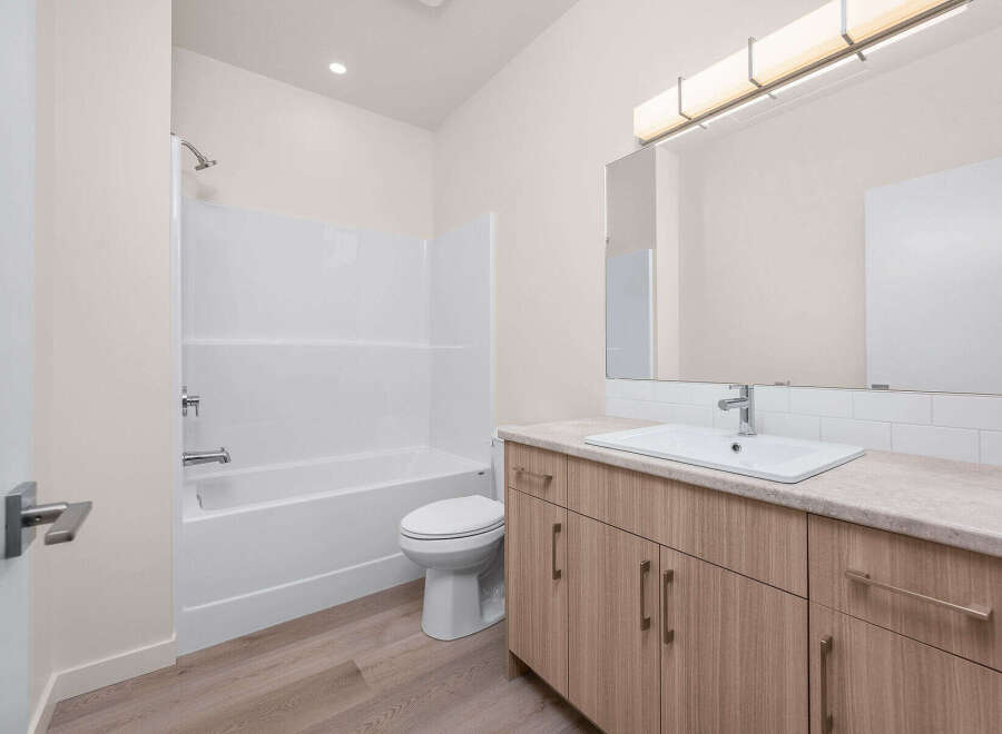 This modern bathroom features a pristine white bathtub and shower combo, complemented by a sleek toilet.