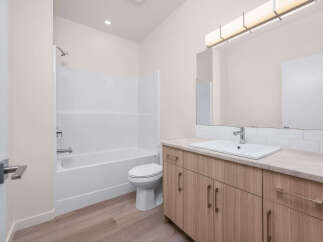 This modern bathroom features a pristine white bathtub and shower combo, complemented by a sleek toilet.