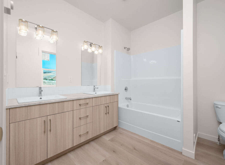 This modern bathroom features a spacious double vanity with ample storage and elegant fixtures, complemented by a pristine white bathtub and shower combo.