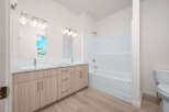 This modern bathroom features a spacious double vanity with ample storage and elegant fixtures, complemented by a pristine white bathtub and shower combo.