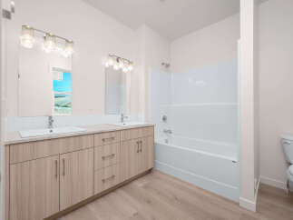 This modern bathroom features a spacious double vanity with ample storage and elegant fixtures, complemented by a pristine white bathtub and shower combo.