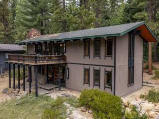 Nestled among tall pine trees, this unique home offers a striking architectural design with a spacious wooden deck perfect for enjoying the serene surroundings.