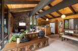Experience rustic charm in this open-concept living space, featuring a striking stone fireplace and exposed wooden beams that create a warm, inviting atmosphere.