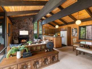 Experience rustic charm in this open-concept living space, featuring a striking stone fireplace and exposed wooden beams that create a warm, inviting atmosphere.