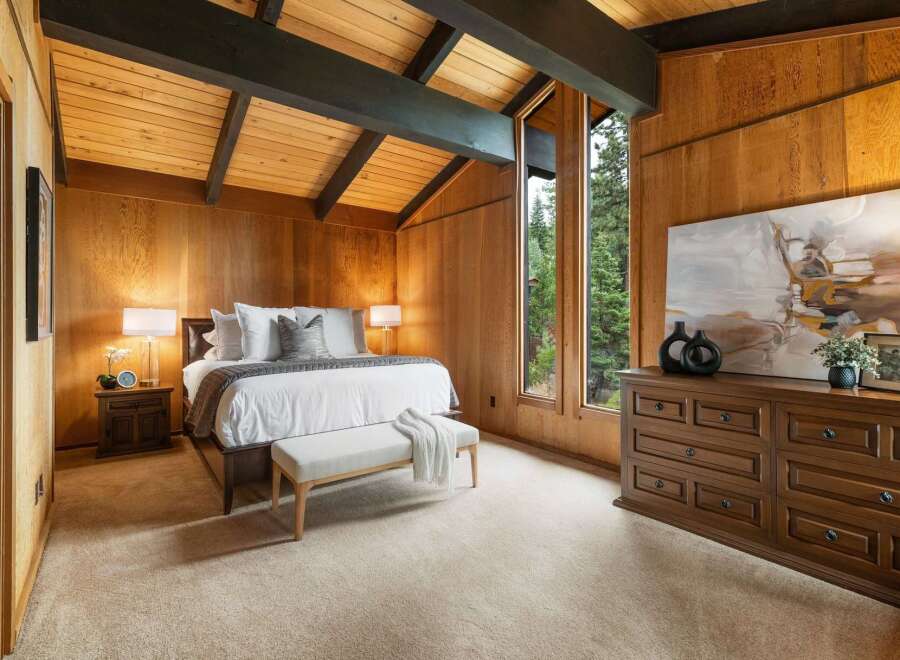 Experience rustic charm in this beautifully appointed bedroom, featuring warm wood paneling and a vaulted ceiling with exposed beams.