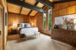 Experience rustic charm in this beautifully appointed bedroom, featuring warm wood paneling and a vaulted ceiling with exposed beams.