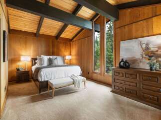 Experience rustic charm in this beautifully appointed bedroom, featuring warm wood paneling and a vaulted ceiling with exposed beams.