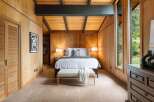 Experience rustic charm in this beautifully appointed bedroom, featuring warm wood-paneled walls and a vaulted ceiling with exposed beams.