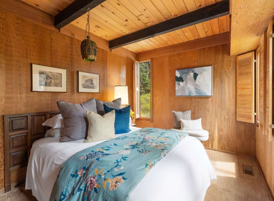 This cozy bedroom features warm wood paneling and a sloped wood-paneled ceiling with exposed beams.