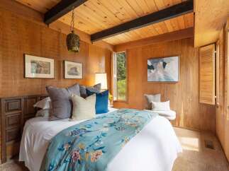 This cozy bedroom features warm wood paneling and a sloped wood-paneled ceiling with exposed beams.