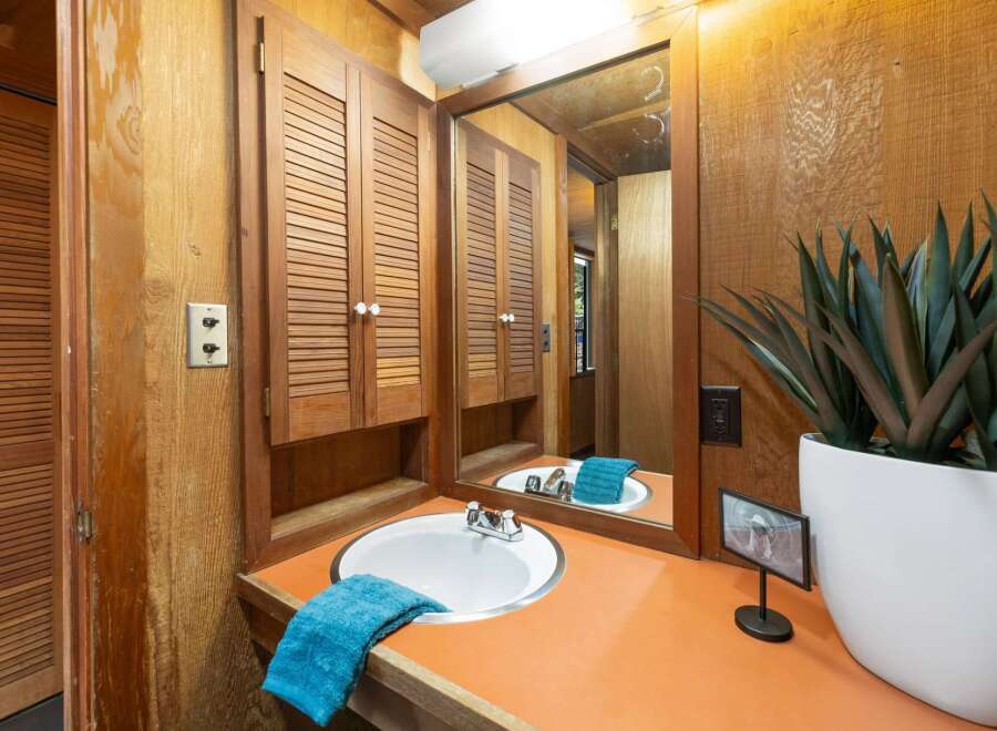 This bathroom features a charming vanity with a white sink and a vibrant orange countertop, complemented by louvered wood cabinets for ample storage.