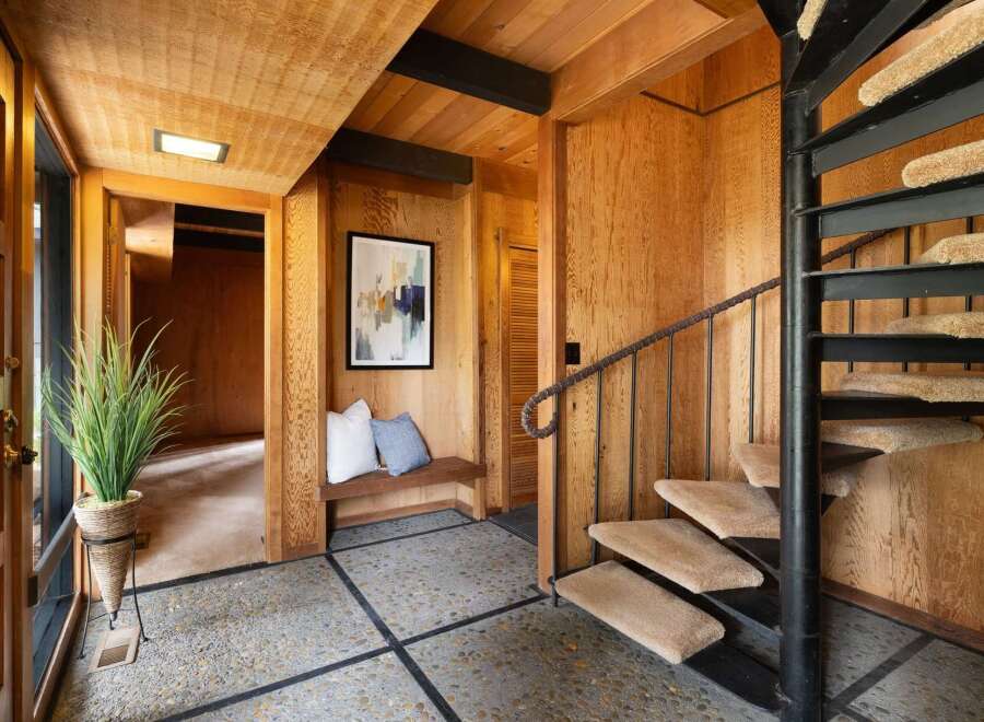 Step into a unique entryway featuring a striking spiral staircase and warm wood paneling throughout.