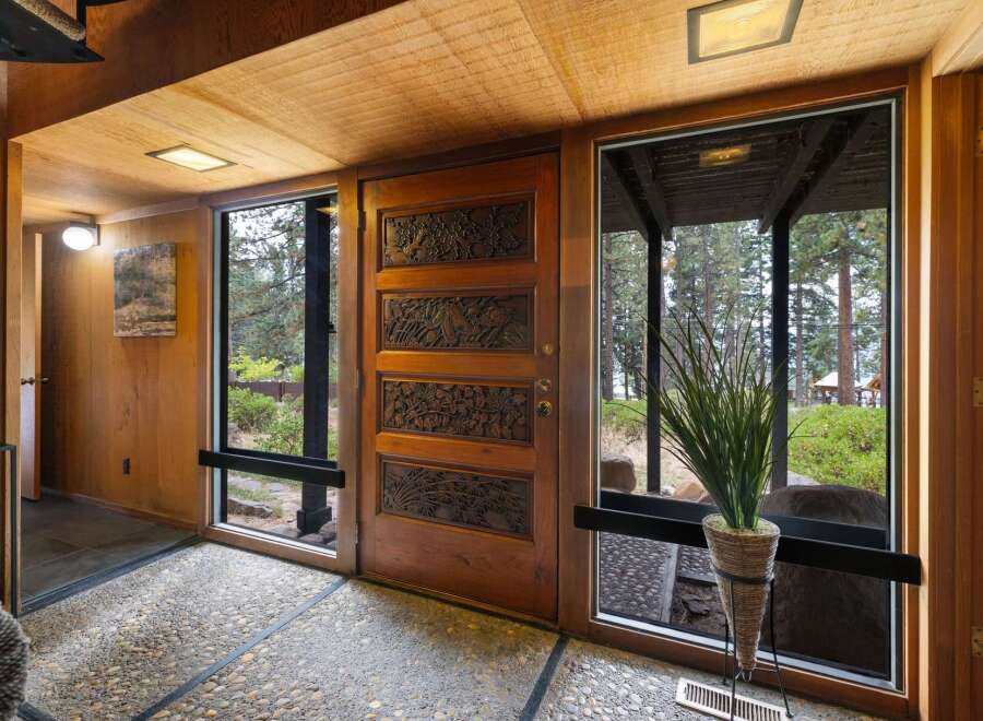 Step into this unique entryway featuring a stunning carved wood door, complemented by natural wood paneling and a textured pebble floor.