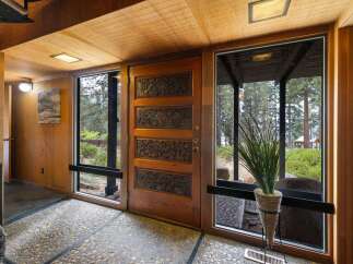 Step into this unique entryway featuring a stunning carved wood door, complemented by natural wood paneling and a textured pebble floor.