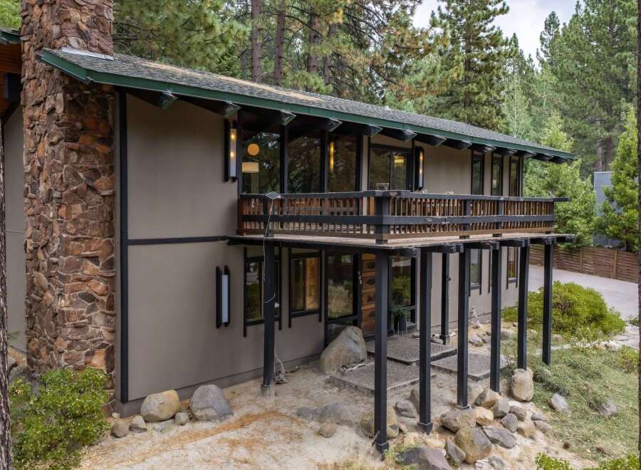 Experience mountain living in this stunning home featuring a prominent stone chimney and expansive wooden deck perfect for enjoying the surrounding pine forest.