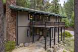 Experience mountain living in this stunning home featuring a prominent stone chimney and expansive wooden deck perfect for enjoying the surrounding pine forest.