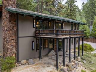 Experience mountain living in this stunning home featuring a prominent stone chimney and expansive wooden deck perfect for enjoying the surrounding pine forest.