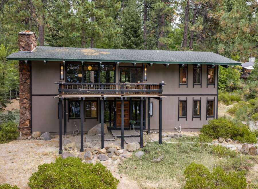 Nestled amidst towering pine trees, this unique home offers a serene retreat with its rustic stone chimney and expansive wooden deck.
