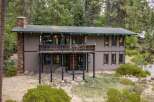 Nestled amidst towering pine trees, this unique home offers a serene retreat with its rustic stone chimney and expansive wooden deck.