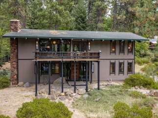Nestled amidst towering pine trees, this unique home offers a serene retreat with its rustic stone chimney and expansive wooden deck.