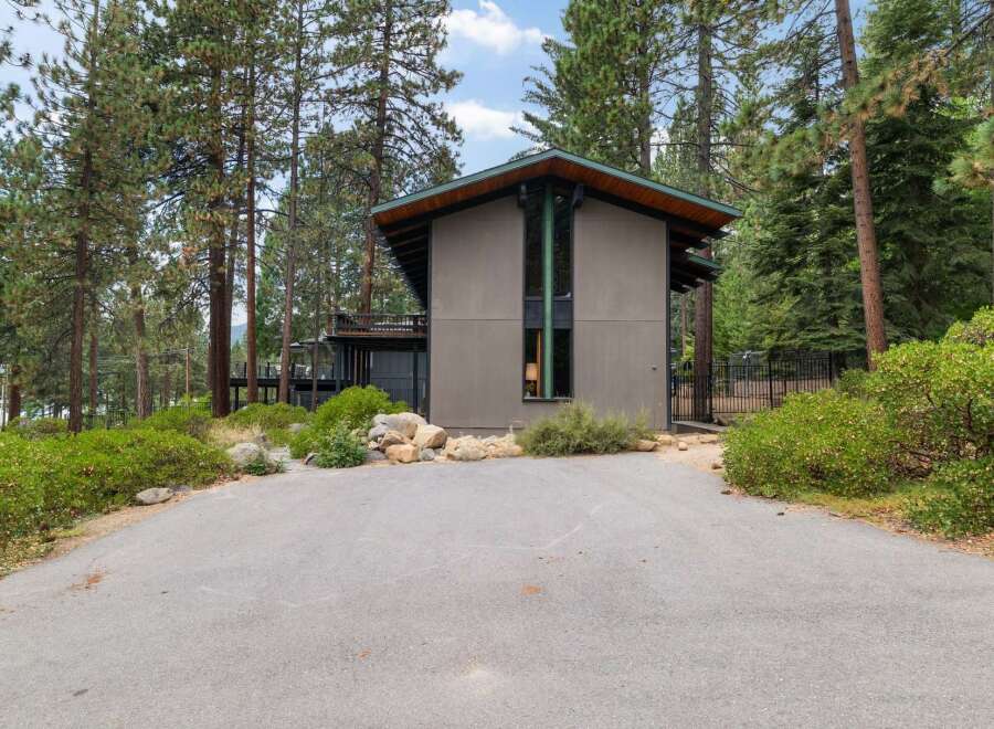 Nestled amidst tall pine trees, this modern home offers a unique architectural design with a striking facade and expansive windows.