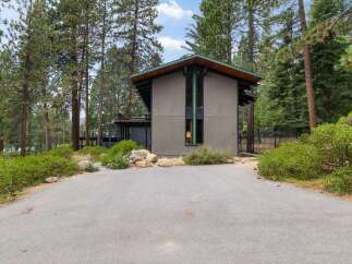 Nestled amidst tall pine trees, this modern home offers a unique architectural design with a striking facade and expansive windows.